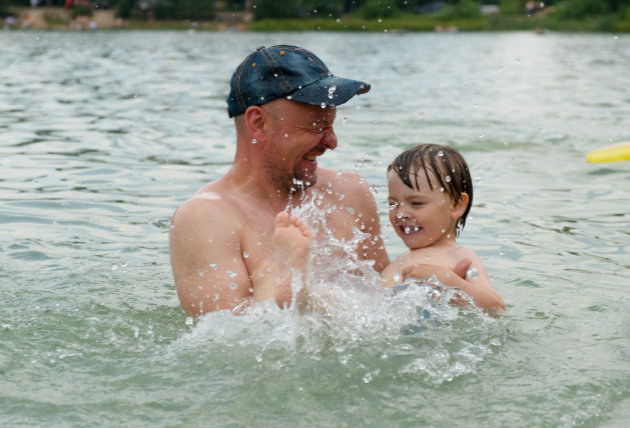 Father and small child having fun swimming in lake in summer